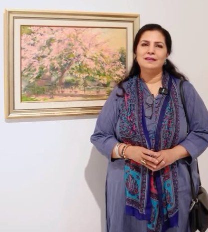 Naela Aamir standing beside one of her framed blossom paintings at an exhibition